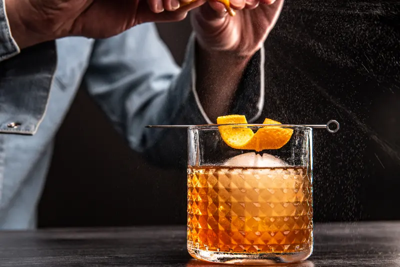 person-zesting-an-old-fashioned-cocktail-drink-2024-12-05-18-13-30-utc